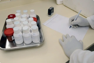 Lab technician writing on a blank form next to prescription bottles on a steel tray, highlighting limited RSV drug supply.