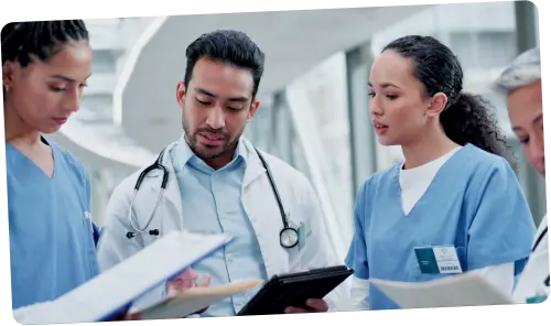 Locum tenens doctors with nurses reviewing charts in a medical unit hallway – xLocums provides tailored locum tenens staffing solutions for hospitals.